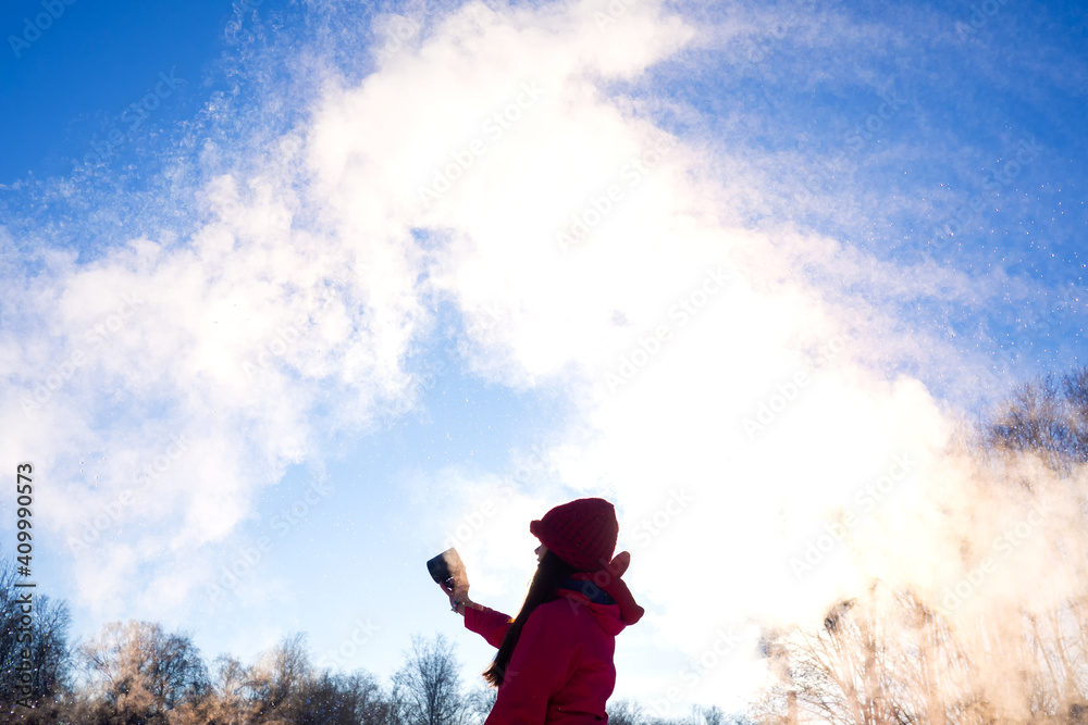 person pouring hot water up in the sky, sunny winter day. Boiling water