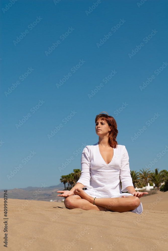 Fototapeta premium woman dressed in white performing meditation and yoga postures on the sand dunes on sunny day