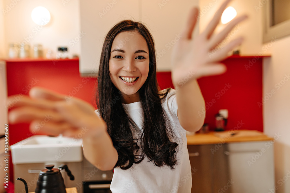 Woman in great mood looks into camera, laughs and claps. Snapshot of girl in white T-shirt in kitchen