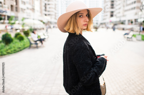 Elegant stylish blonde short hair girl in hat posing with coffee over street background