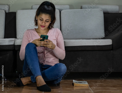 Young woman sitting on the floor typing on her cell phone