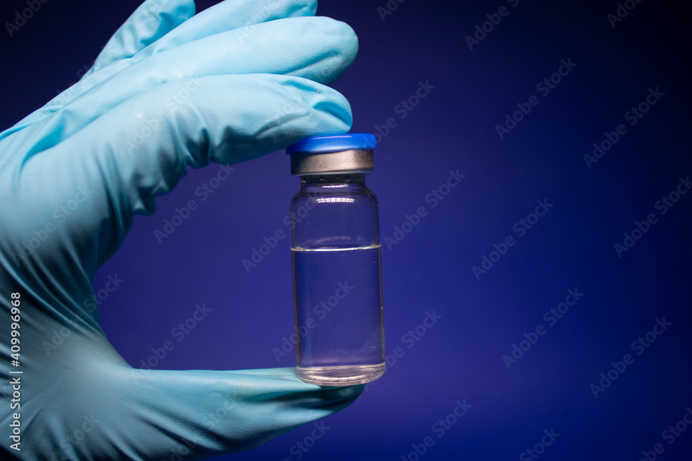 Development of coronavirus vaccine COVID-19. bottle phial with no label in blue medical glove. isolated on blue background. cure. Vaccination for prevention and treatment to infections Development of coronavirus vaccine COVID-19. bottle phial with no label in blue medical glove. isolated on blue background. cure. Vaccination for prevention and treatment to infections