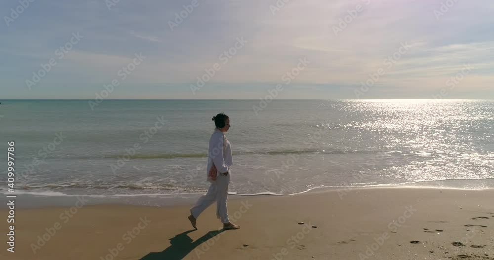 Mujer median aedad paseando por la playa escuchando música en audífonos