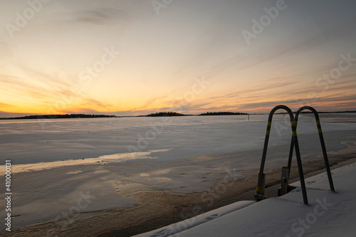 Empty dock ladder for winter swimming in the frozen lake this morning during sunrise. Lake covered in snow and ice. Photo taken in Vasteras, Sweden.