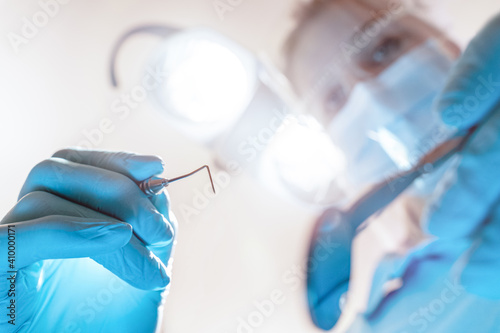 Zahnarzt / Zahnärztin mit Sonde und OP Leuchte aus Sicht des Patienten dicht über dem Mund bei der Untersuchung mit Corona Maske