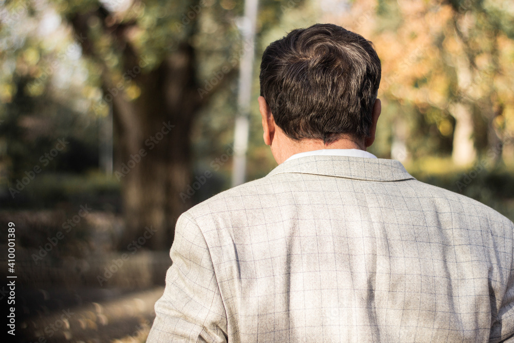 Senior man walking, hands clasped. Senior man walking and relaxing in park. Walking away, relaxing, rear view