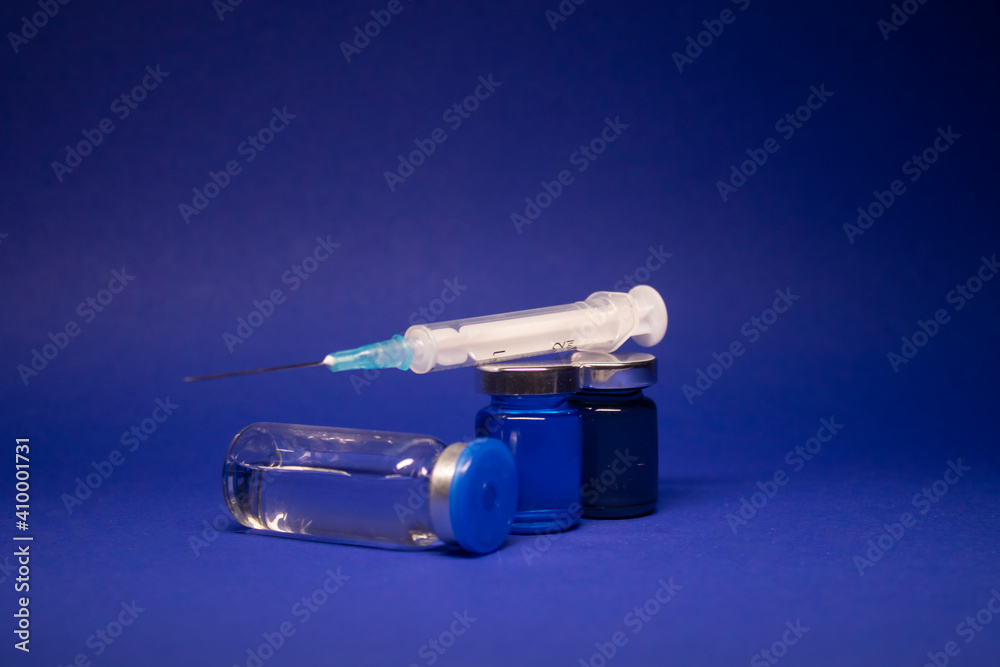 three transparent Vaccine bottle phial with no label, medical syringe injection needle. isolated on blue background. Development of coronavirus vaccine COVID-19. cure. World race in researching three transparent Vaccine bottle phial with no label, medical syringe injection needle. isolated on blue background. Development of coronavirus vaccine COVID-19. cure. World race in researching
