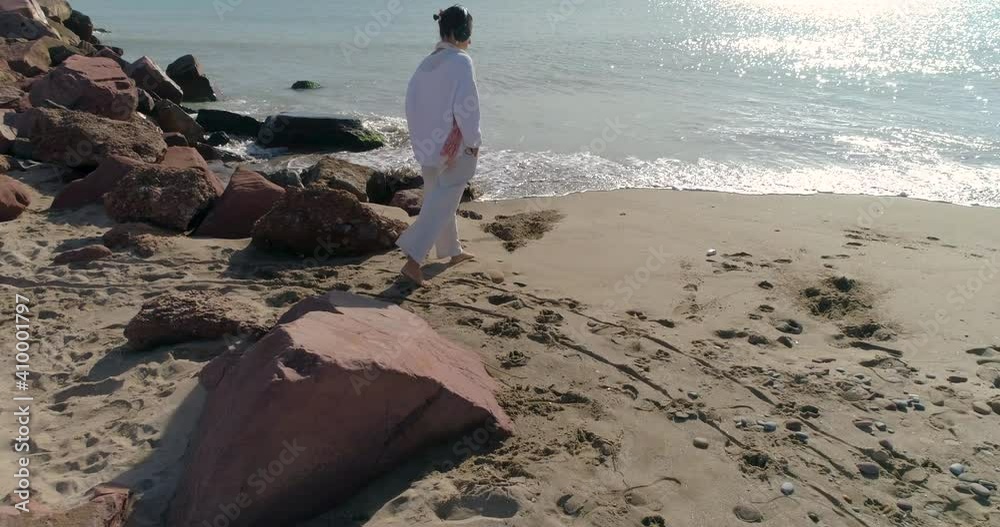 dron volando paralelamente a mujer paseando por la playa vestida de blanco