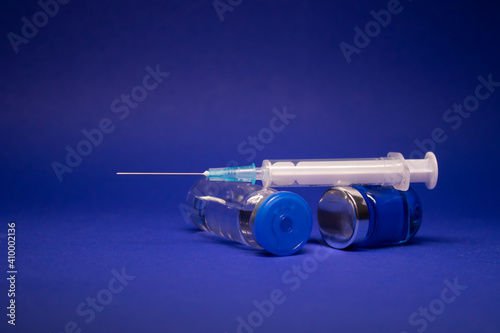 two transparent Vaccine bottle phial with no label, medical syringe injection needle. isolated on blue background. Development of coronavirus vaccine COVID-19. cure. World race in researching