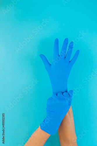 Two hands on a blue background putting on blue latex gloves