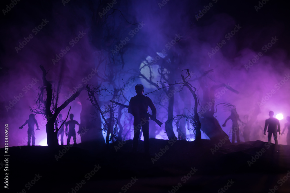 Man with riffle against zombie attack. Zombie apocalypse. Scary view of blurred zombies at cemetery and spooky cloudy sky with fog. Horror Halloween concept.