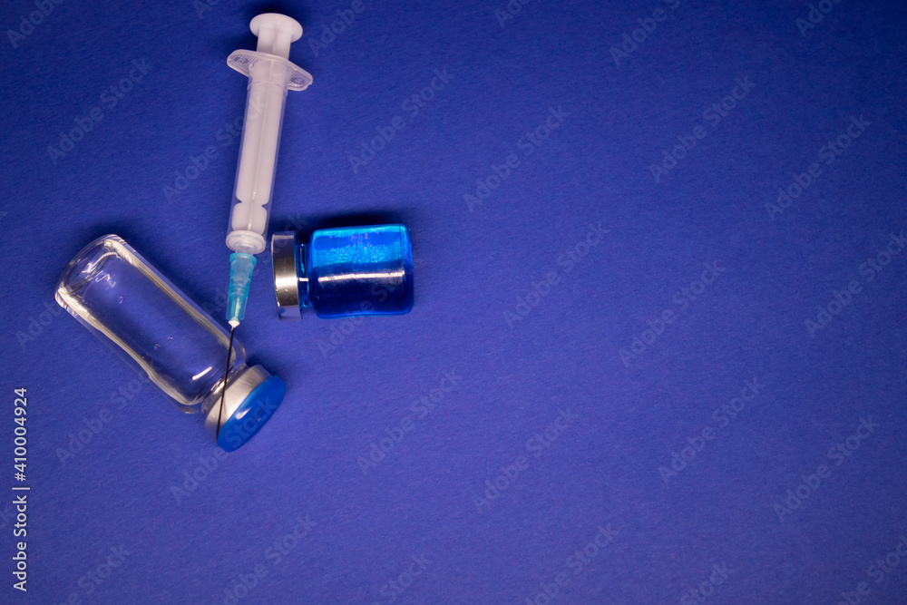 two transparent Vaccine bottle phial with no label, medical syringe injection needle. isolated on blue background. Development of coronavirus vaccine COVID-19. cure. World race in researching