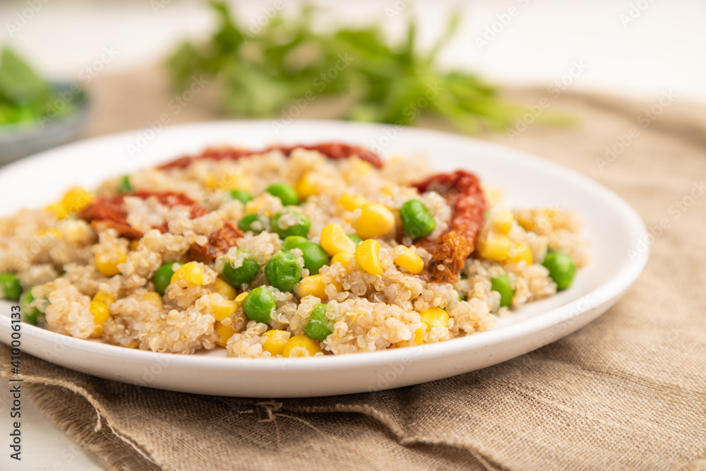 Quinoa porridge with green pea, corn and dried tomatoes on ceramic plate on a white wooden background. Side view, selective focus.