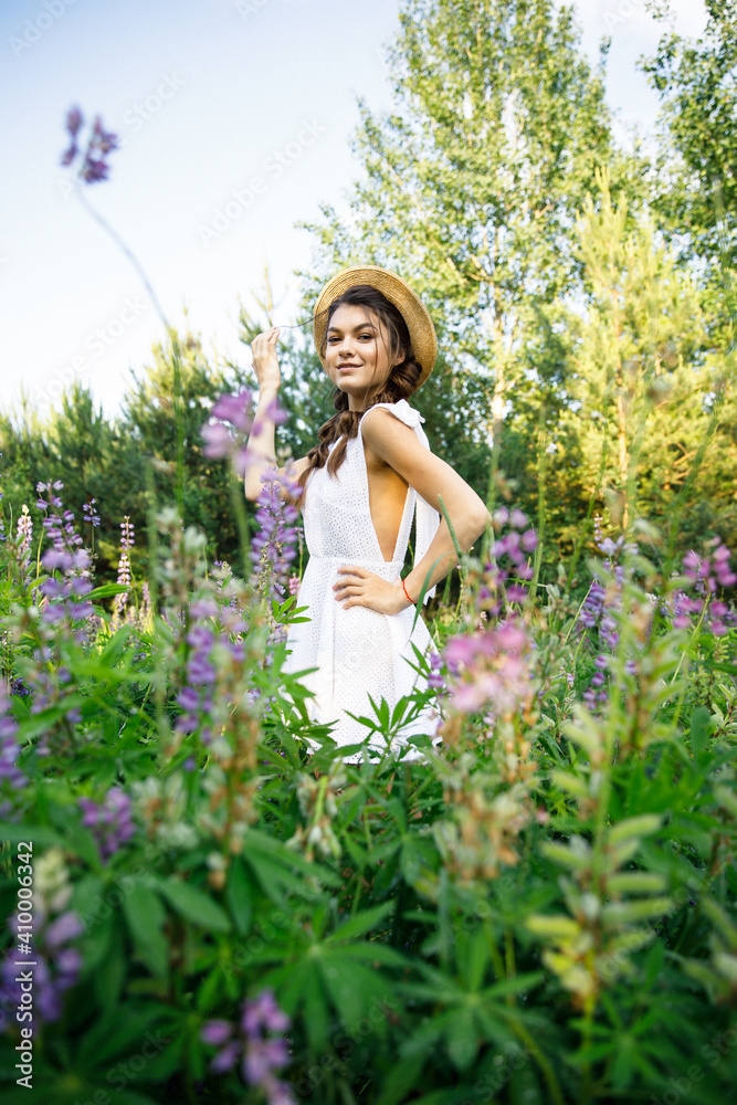 a young beautiful girl in a white dress and hat walks across the field with lupins a young beautiful girl in a white dress and hat walks across the field with lupins