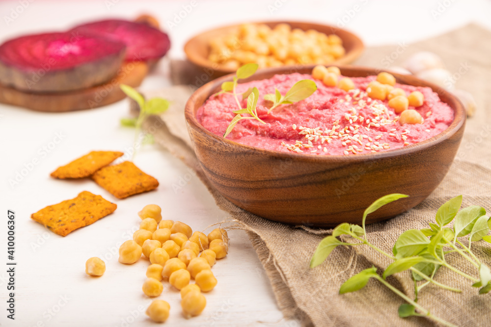 Hummus with beet and microgreen basil sprouts in wooden bowl on a white wooden background. Side view, selective focus. Hummus with beet and microgreen basil sprouts in wooden bowl on a white wooden background. Side view, selective focus.