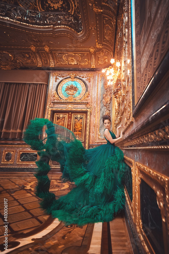 Portrait of a beautiful young girl in a Haute couture green dress standing in a luxurious gold interior.