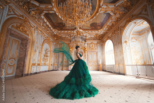 Portrait of a beautiful young girl in a Haute couture green dress standing in a luxurious gold interior. photo