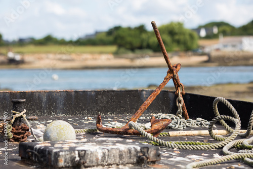 Rusted anchor on fishing boat in Morbihan, Brittany, France. With ocean and coastline in the background.