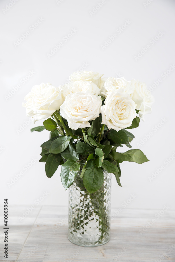 Fototapeta premium Bouquet of white roses in a glass vase on a beige table against a gray wall. Copy space.