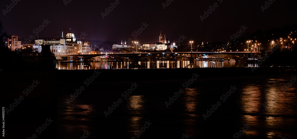 .panoramic view of Prague Castle and St. Vitus Cathedral and the Vltava River and street lights on bridges at night in the center of Prague
