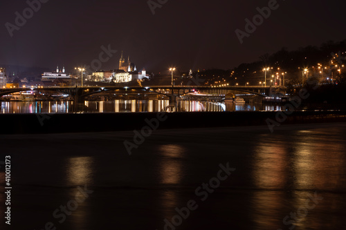 .panoramic view of Prague Castle and St. Vitus Cathedral and the Vltava River and street lights on bridges at night in the center of Prague