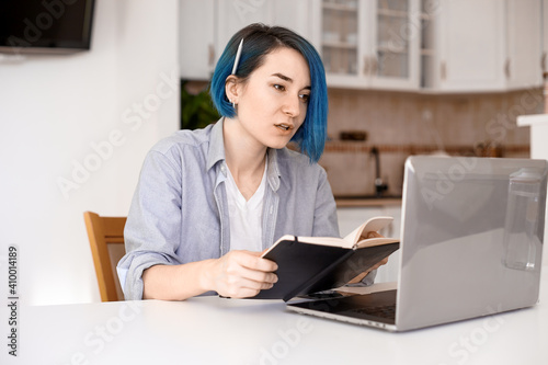 Smiling women with blue hair working long hours from her home office. Student girl working at home. Work or study from home, freelance, business.