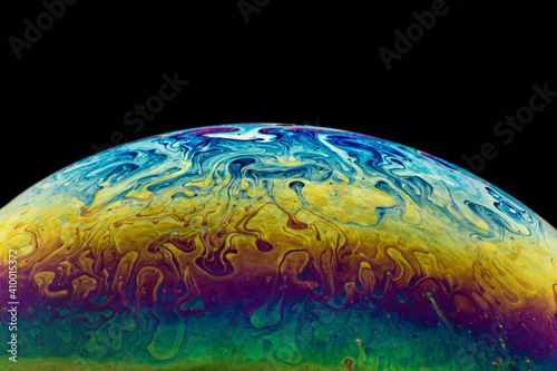 Side of a soap bubble macro, close up detailed shot. Bright, rainbow colors looking like a imitation of space, planet on black background. 