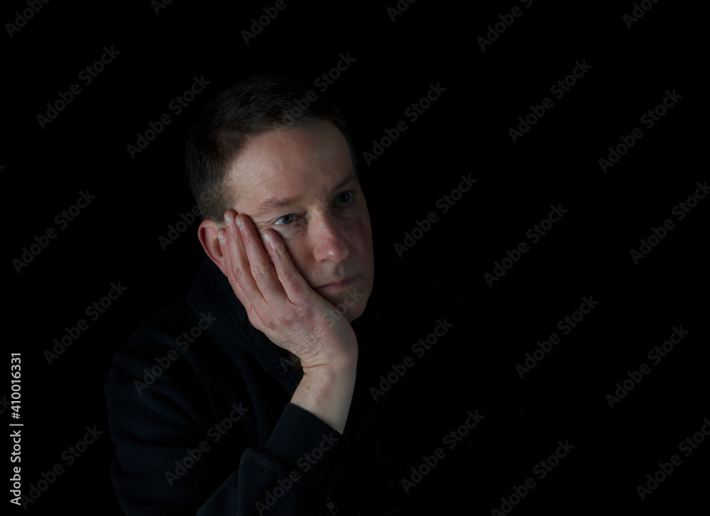Depressed mature man holding his cheek in the dark while looking sad Depressed mature man holding his cheek in the dark while looking sad