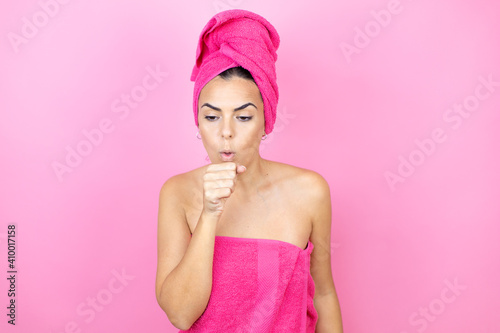 Young beautiful woman wearing shower towel after bath standing over isolated pink background with her hand to her mouth because she's coughing