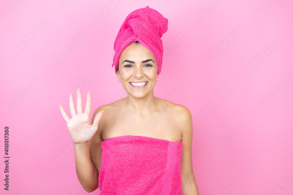Young beautiful woman wearing shower towel after bath standing over isolated pink background showing and pointing up with fingers number five while smiling confident and happy