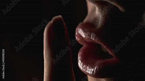Gesture of shhh, secret, silence. Close-up view of woman face, she holding finger on her lips over black background.
