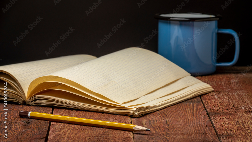 Naklejka premium old blank notebook or travel journal opened on a rustic wood table with a metal cup of tea