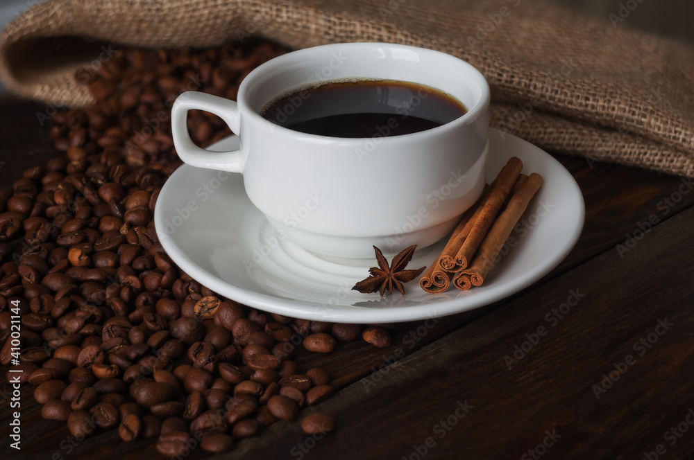 A cup of coffee, roasted coffee beans, cinnamon sticks and star anise on a wooden table. A cup of coffee, roasted coffee beans, cinnamon sticks and star anise on a wooden table.