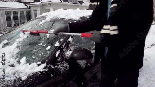 Man in Dark Coat removes Ice from a Black Car
