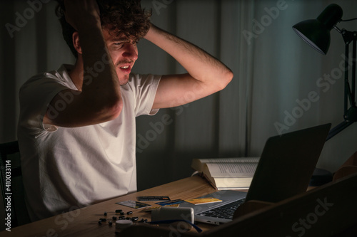 man sitting at night with labtop and sleepng pills and credit cards on desk photo