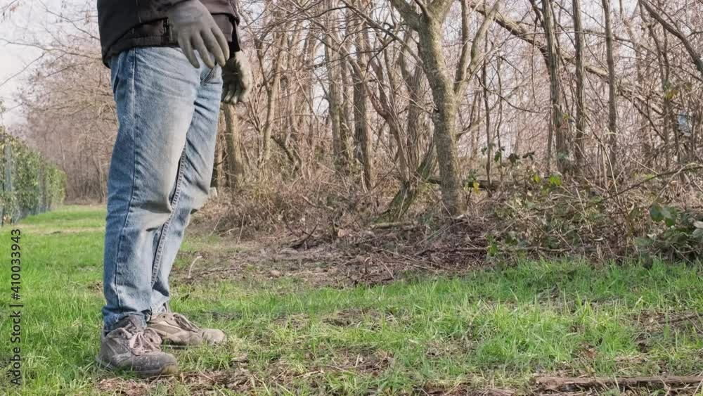 Man In Blue Jeans With Black Jacket And Gloves Standing In Front Of The Woods During Sunny Winter Day - Static Close Up View Man In Blue Jeans With Black Jacket And Gloves Standing In Front Of The Woods During Sunny Winter Day - Static Close Up View