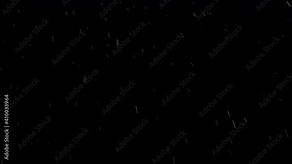 Shiny raindrops falling against dark black night background as moving particles.
