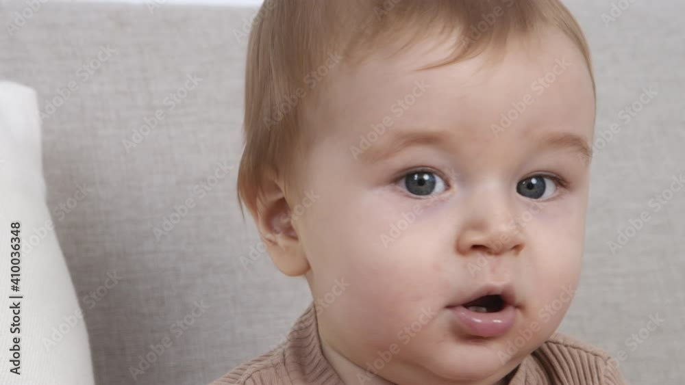 Portrait of cute 6 months baby sitting on sofa, looking emotionally, slow motion Portrait of cute 6 months baby sitting on sofa, looking emotionally, slow motion