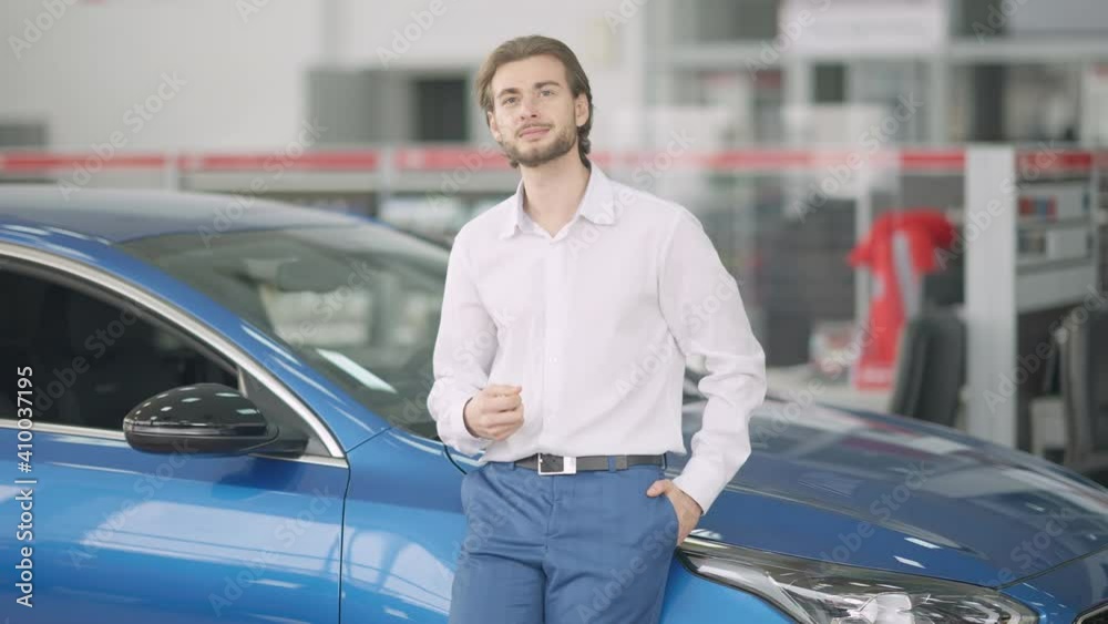 Portrait of rich confident Caucasian young man posing at new blue car in dealership. Smiling handsome wealthy businessman throwing and catching keys looking at camera. Success and luxury concept. Portrait of rich confident Caucasian young man posing at new blue car in dealership. Smiling handsome wealthy businessman throwing and catching keys looking at camera. Success and luxury concept.