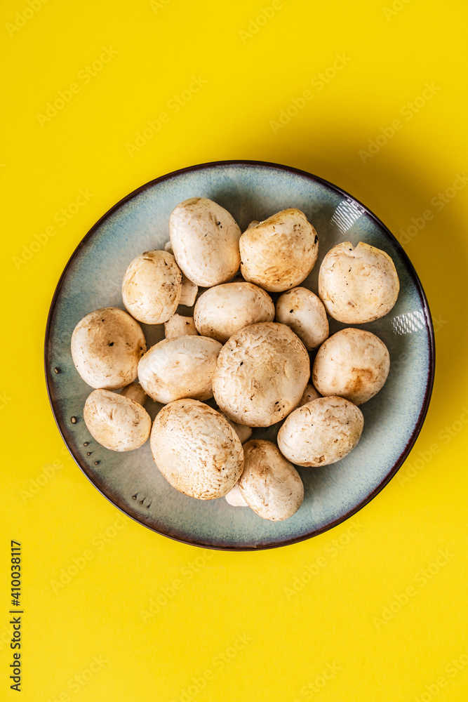 Fototapeta premium Top view on plate with white common champignon mushrooms on yellow background