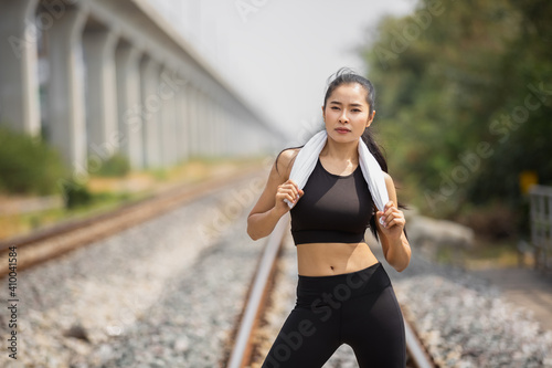 Asian young woman tan skin in black sportswear outdoor physical exercises for successfull health at railway side and eye contact to camera.