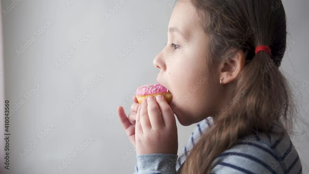 Little caucasian girl eating pink donuts. Enjoying. Close up. Little caucasian girl eating pink donuts. Enjoying. Close up.