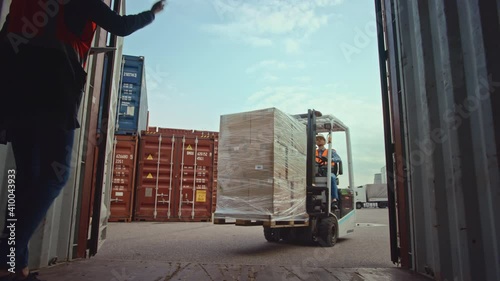 Forklift Driver Loading a Shipping Cargo Container with a Full Pallet with Carboard Boxes in Logistics Operations Port Terminal. Female Industrial Supervisor and Safety Inspector Helping the Process.