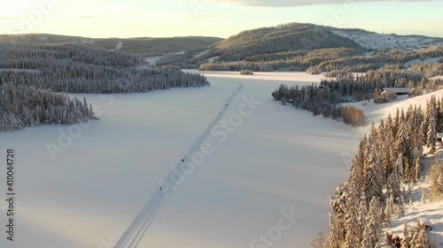 High altitude aerial view of skiers on frozen lake and mountains in the background.