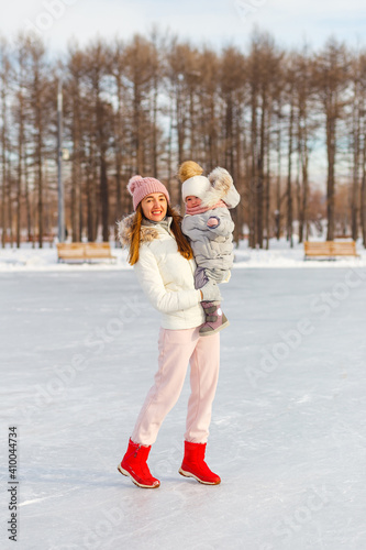 Happy young woman and one-and-a-half-year-old girl in winter in warm jackets walk in the park. mother and daughter in winter clothes