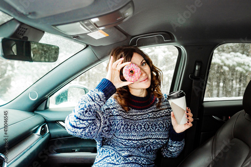 Woman eating a sweet donut and drinking coffee sitting in a car 