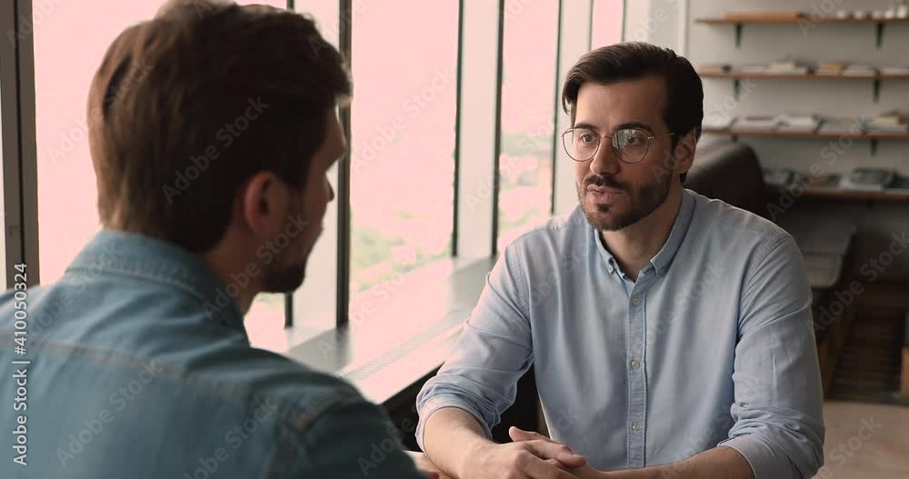 Rear back view smart young confident male hr manager employer holding job interview meeting with skilled vacancy candidate, asking about working experience, describing position talking in office.