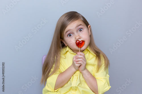 valentine's day caucasian child holding a lollipop heart over grey background.Surprised face.Donation,heart health,world heart day, world health day,world mental health day.Health and heart concept.