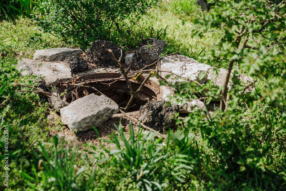 A deep, old, uncovered manhole is dangerous for pedestrians and animals. Instead of a cover, warning tree branches stick out from the hatch A deep, old, uncovered manhole is dangerous for pedestrians and animals. Instead of a cover, warning tree branches stick out from the hatch