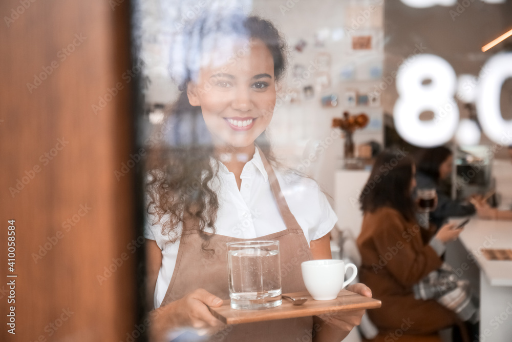 Young barista with cup of hot espresso in cafe, view through glass door Young barista with cup of hot espresso in cafe, view through glass door